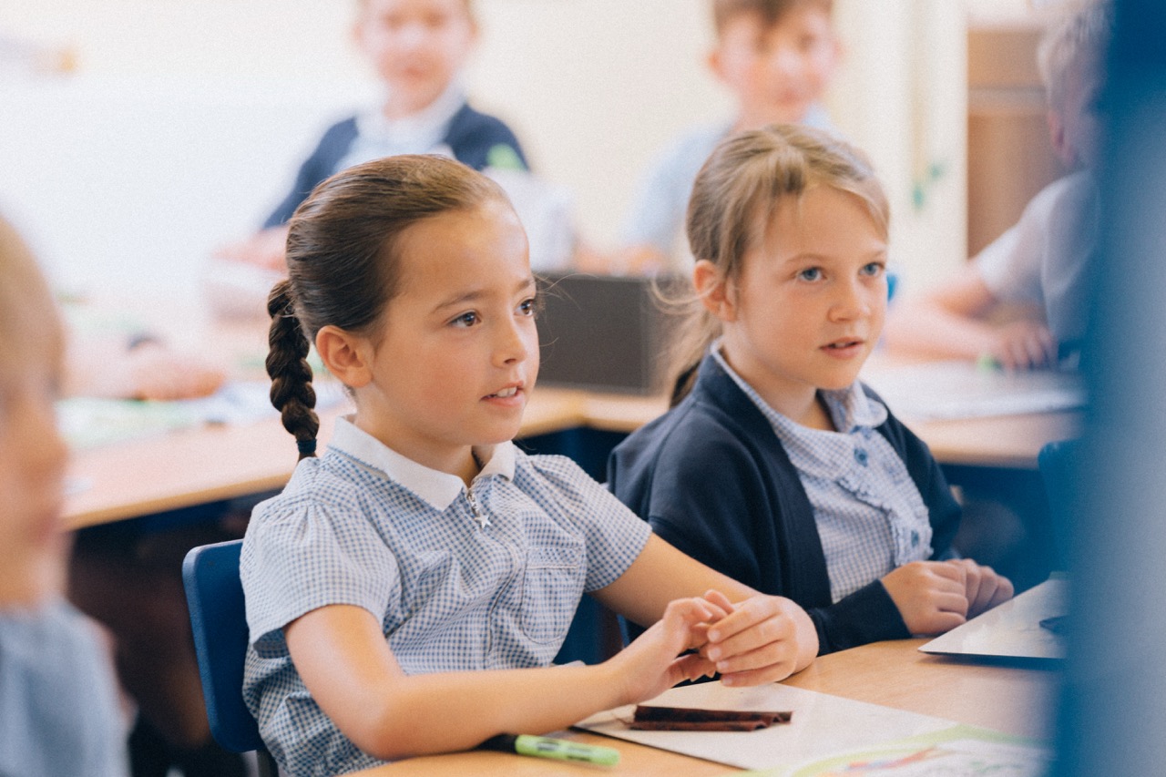 two school girls at their desk focusing on the teacher out of shot in front of them
